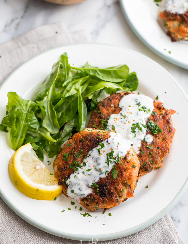Easy salmon patties on white plate with lemon garlic sauce drizzle and salad.