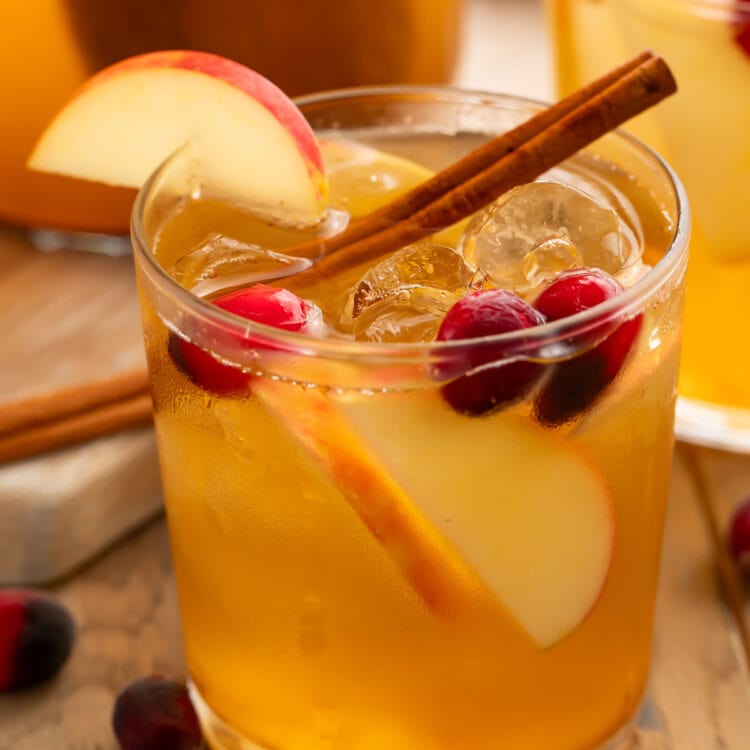 An apple cider sangria in a glass garnished with apples, grapes, and a cinnamon stick.
