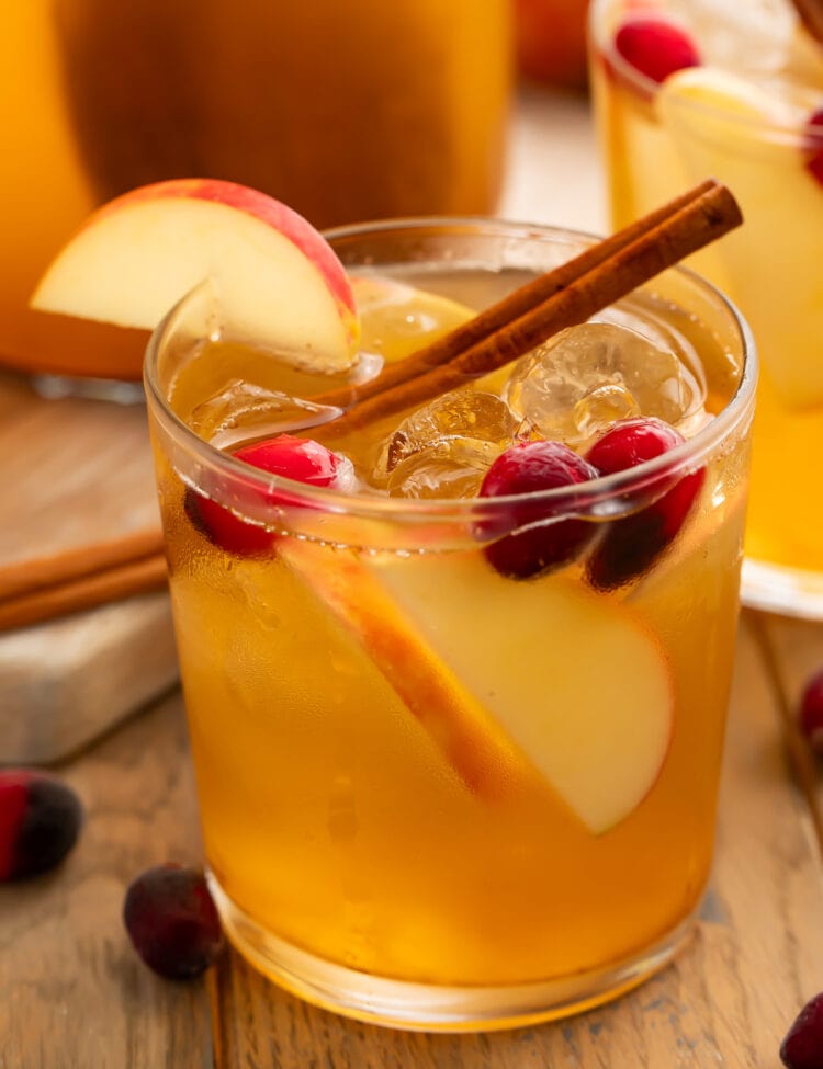 An apple cider sangria in a glass garnished with apples, grapes, and a cinnamon stick.