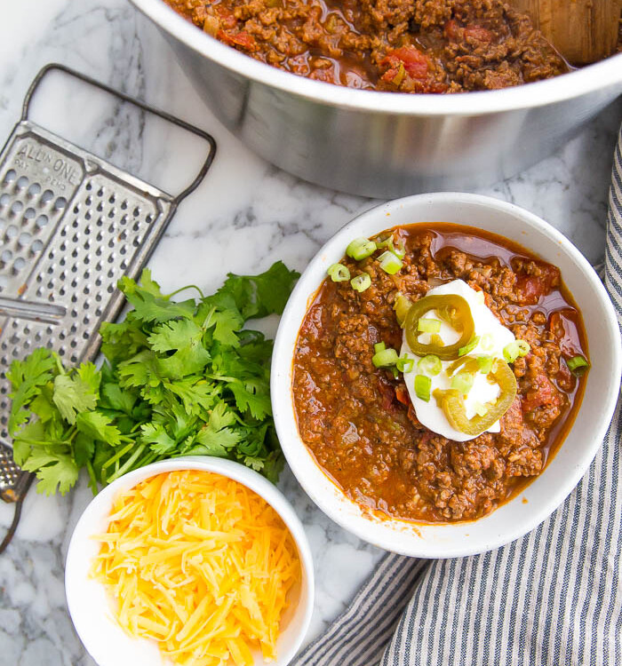 Bowl and pot of low carb chili with cilantro, cheese, sour cream, and jalapeno.