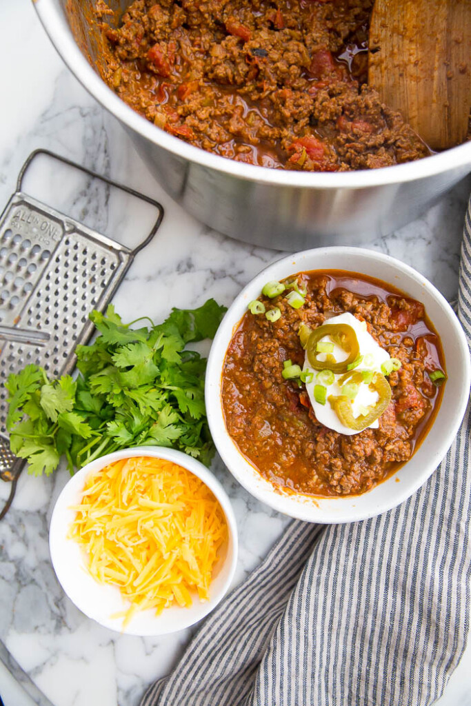 Low Carb Chili in a pot and bowl with sour cream, shredded cheese, cilantro, and green onions. 