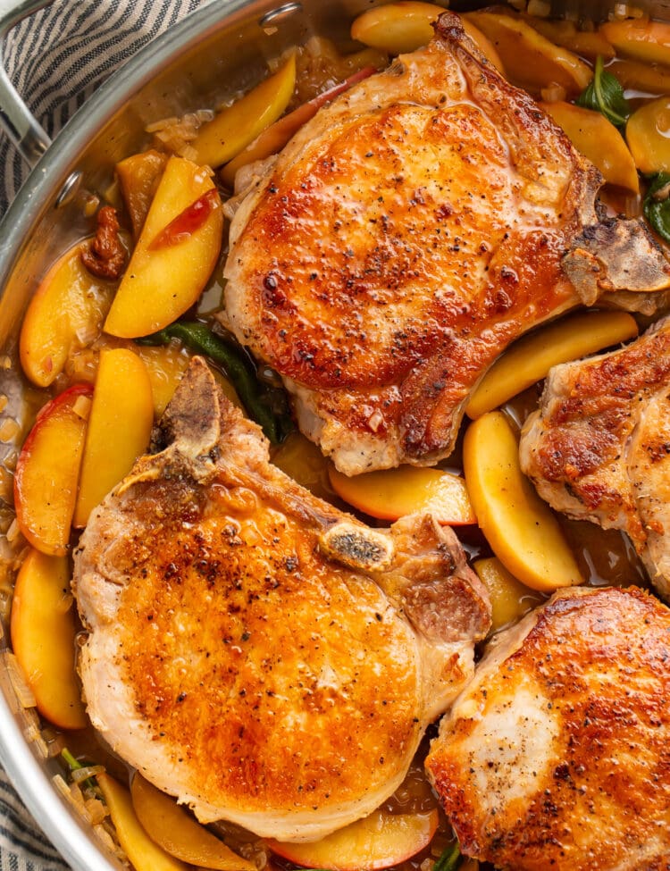 Seared pork chops with apples and a sage butter sauce in a large silver skillet.