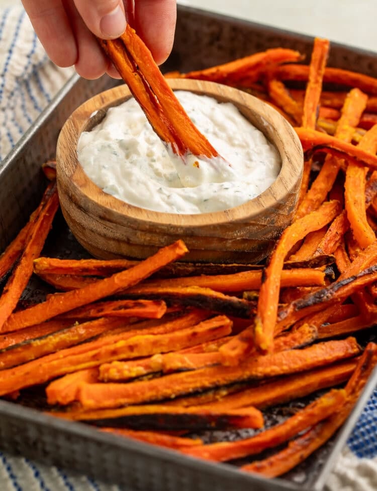 Carrot fry from a tray of them being dipped into a wooden bowl of creamy dip.