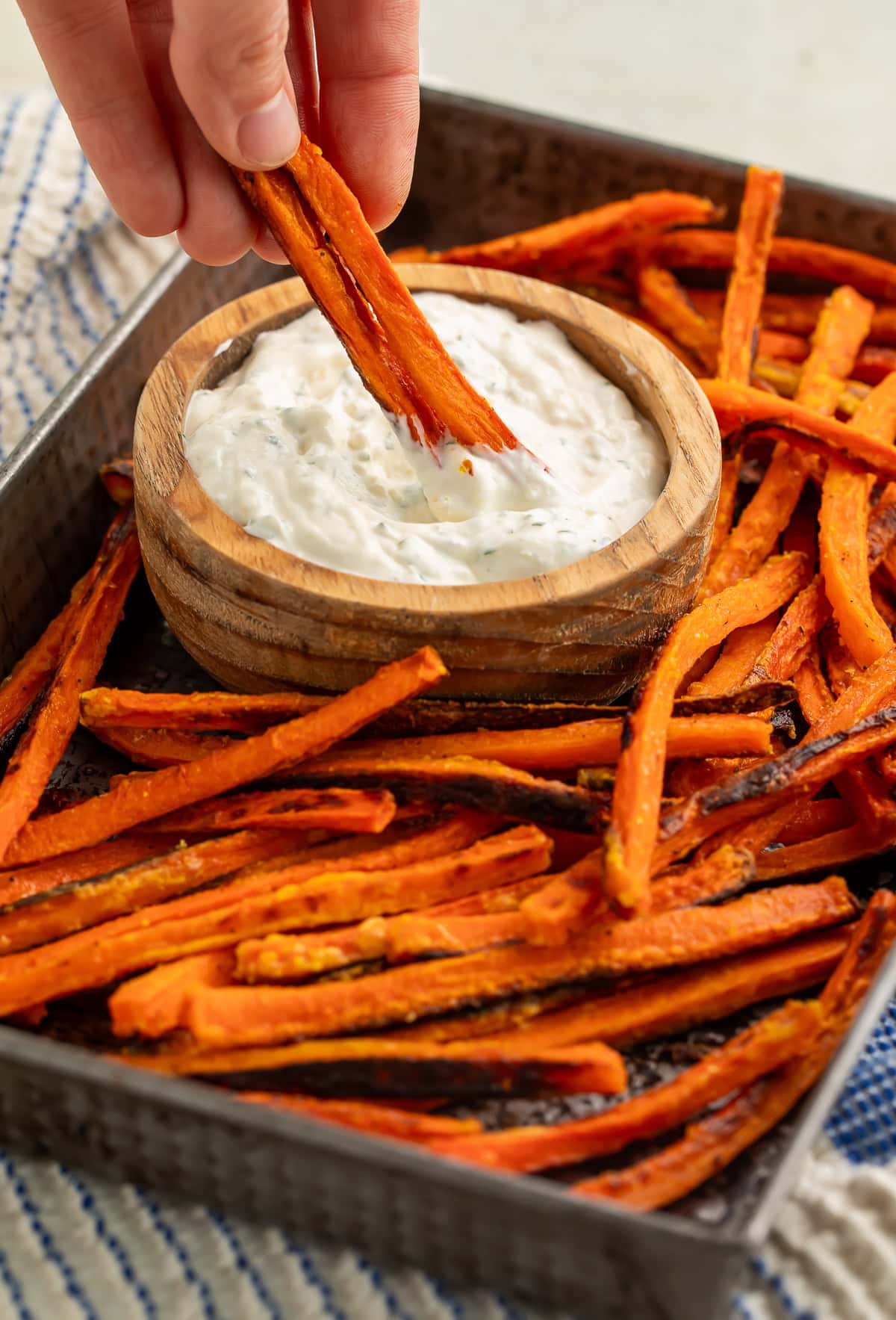 Carrot fry from a tray of them being dipped into a wooden bowl of creamy dip.