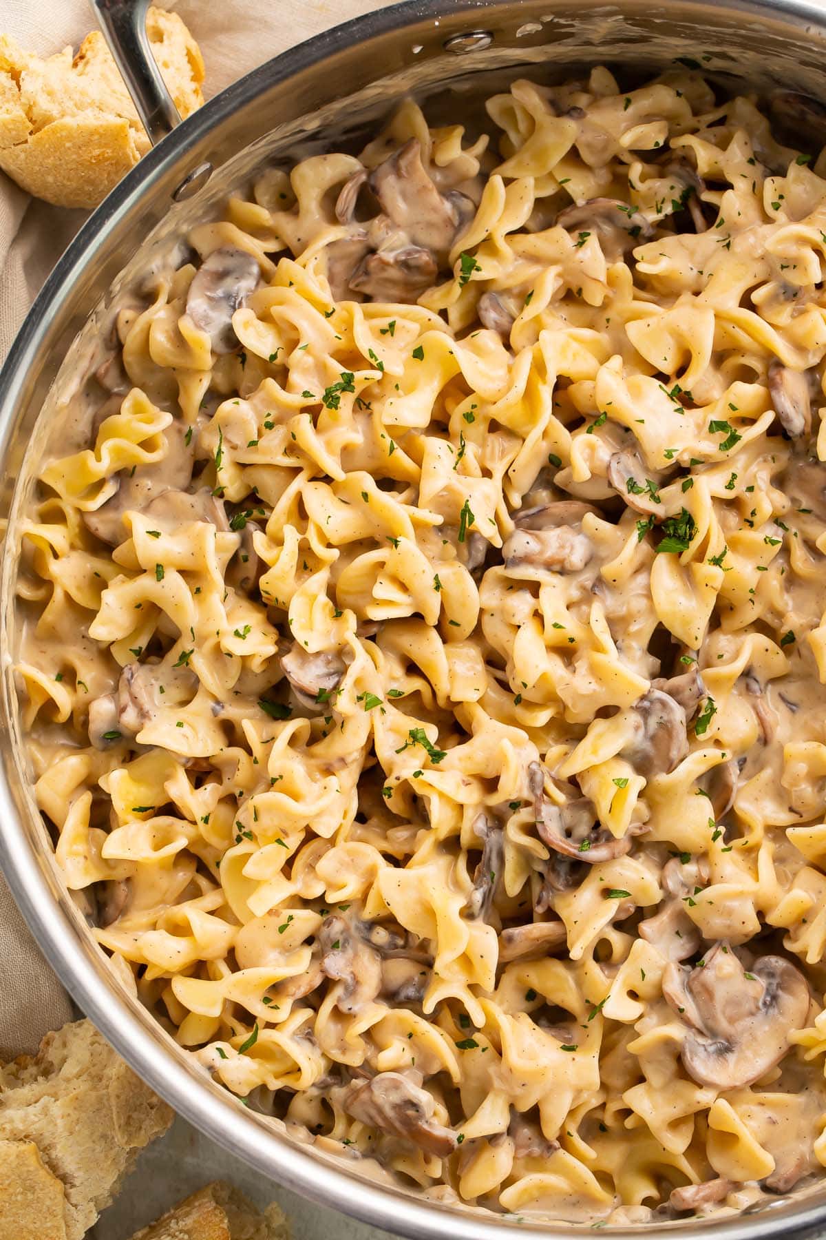 A large stainless skillet holding mushroom stroganoff made with egg noodles and pieces of baby bella mushrooms.