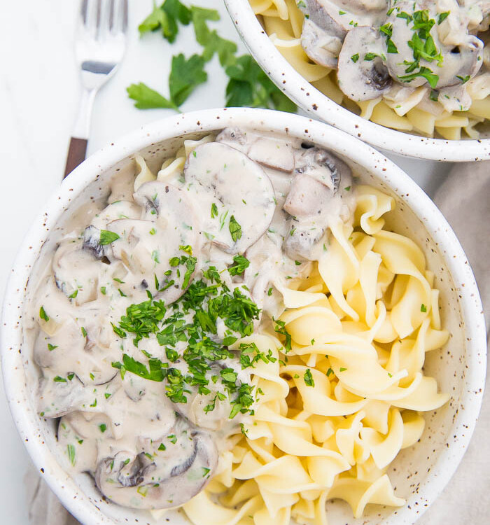 Bowl of mushroom stroganoff in white bowl with egg noodles and fresh parsley