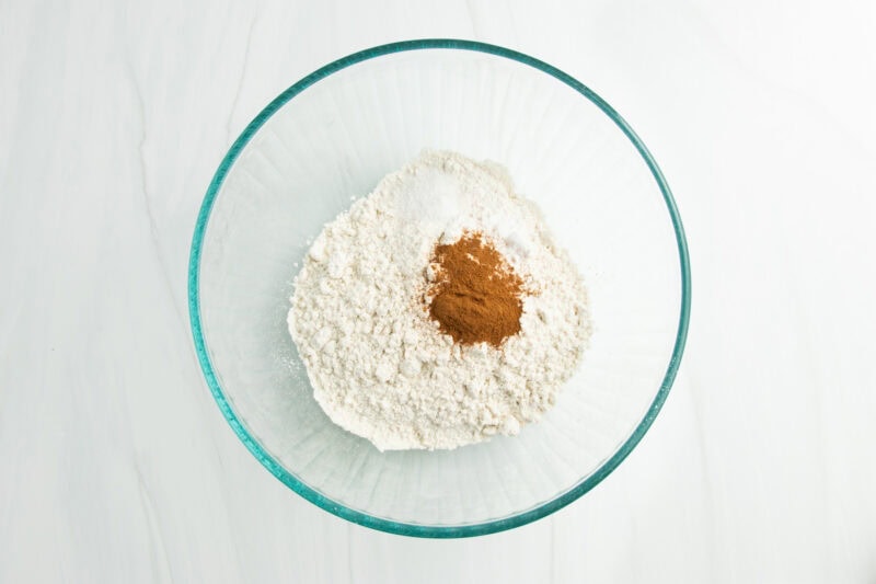 Overhead view of flour, salt, cinnamon, and baking soda in large glass mixing bowl.