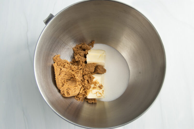 Overhead view of butter, brown sugar, and white sugar in a large metal mixing bowl from a stand mixer.