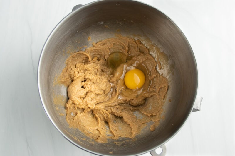 Overhead view of creamed butter and sugar in a stand mixer bowl with one egg, unincorporated.