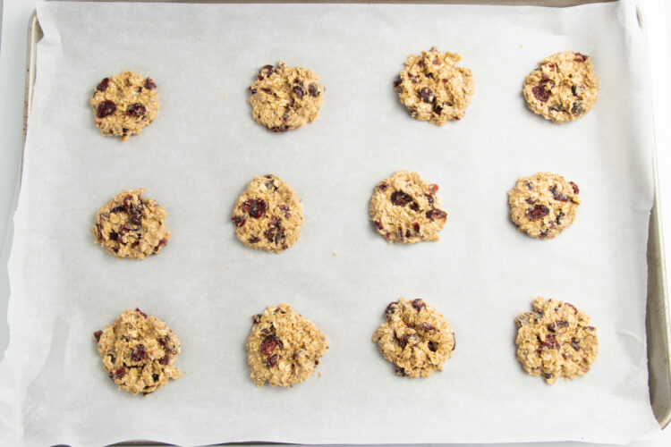 Small unbaked cranberry oatmeal cookies lined 3x4 on a parchment-paper-lined baking sheet.