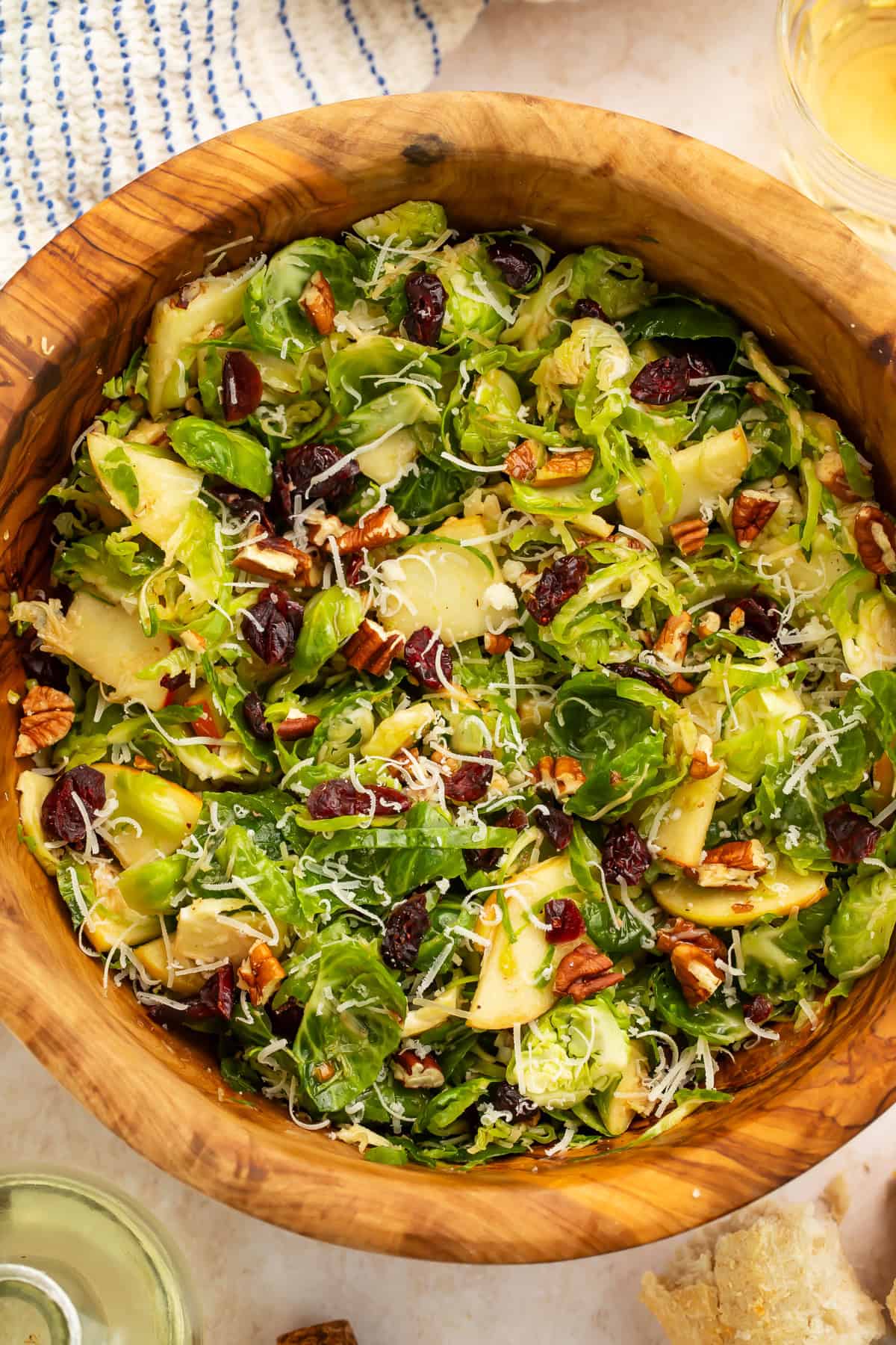 Wooden bowl of shredded brussels sprouts salad with pieces of apple and dried cranberries.