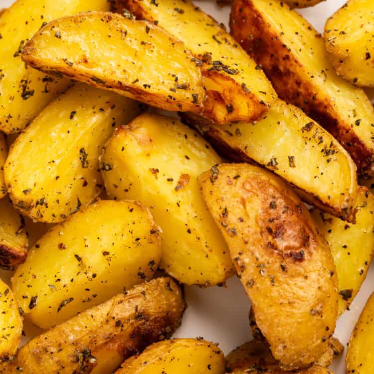 Close up of rosemary roasted potato wedges in a white serving dish.