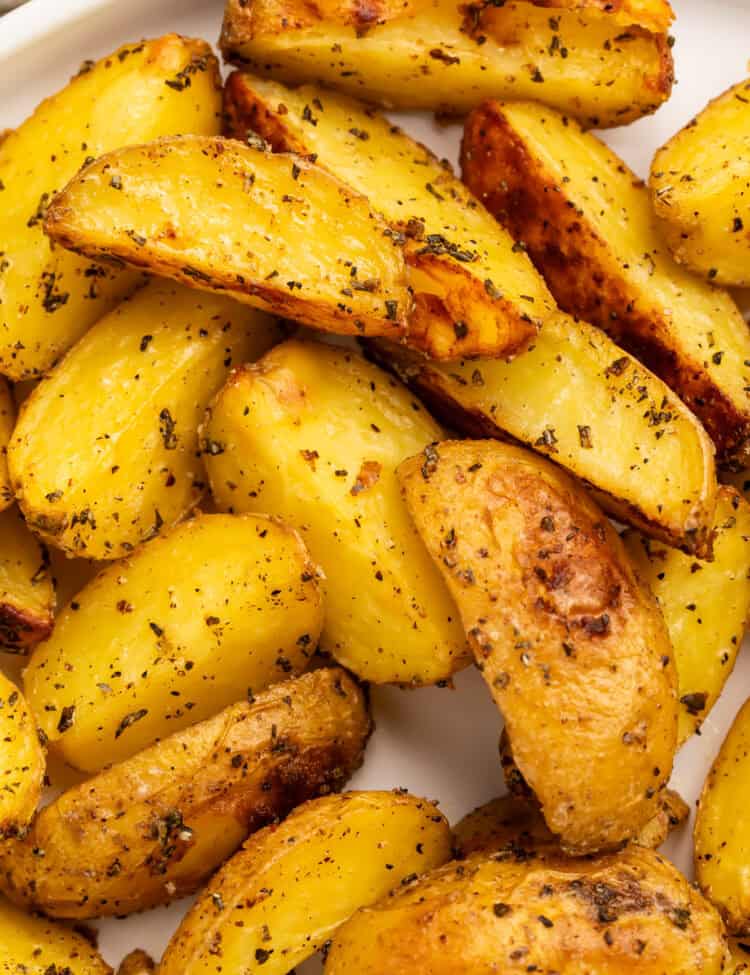 Close up of rosemary roasted potato wedges in a white serving dish.