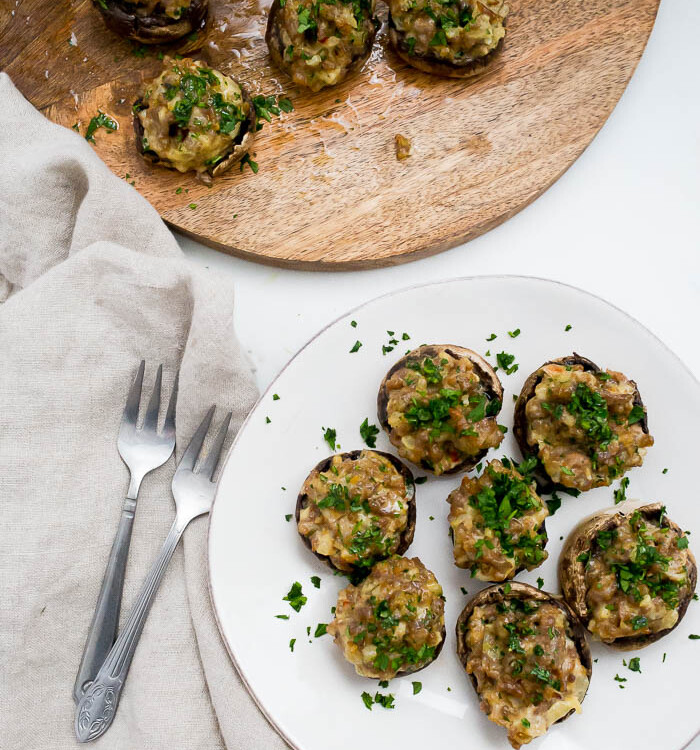 overhead shot of sausage stuffed mushrooms on white plate with parsley