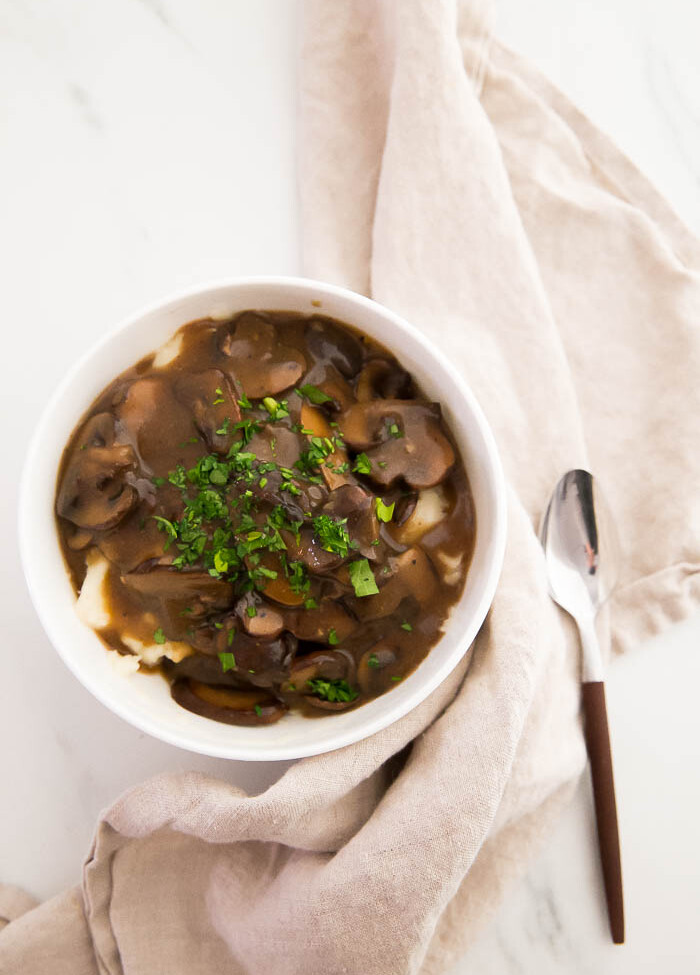 overhead shot of vegan mushroom gravy on top of mashed potatoes in white bowl
