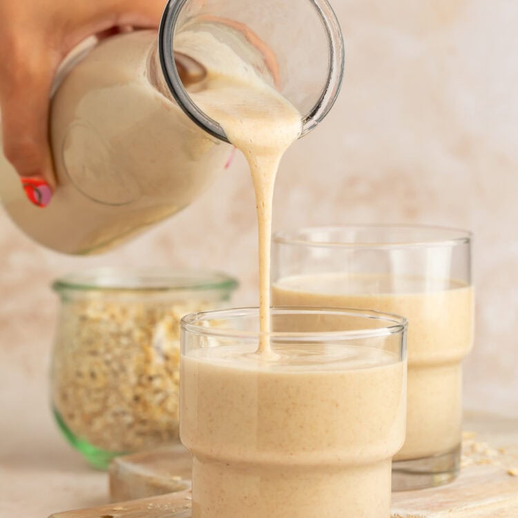 Hand pouring oat milk into a glass from a glass bottle.