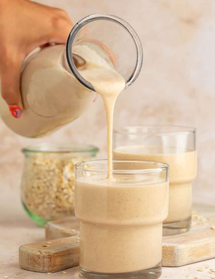 Hand pouring oat milk into a glass from a glass bottle.