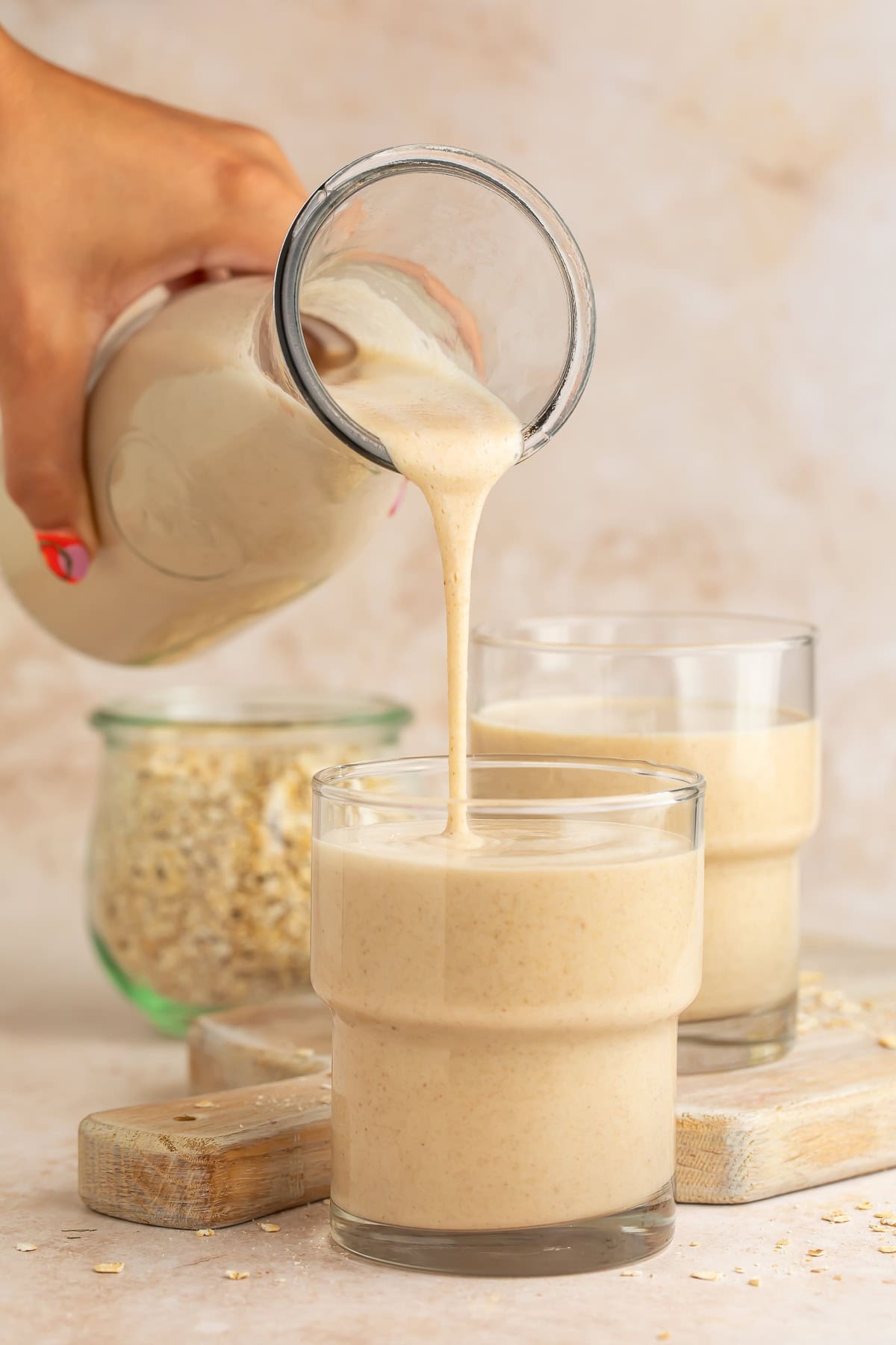 Hand pouring oat milk into a glass from a glass bottle.