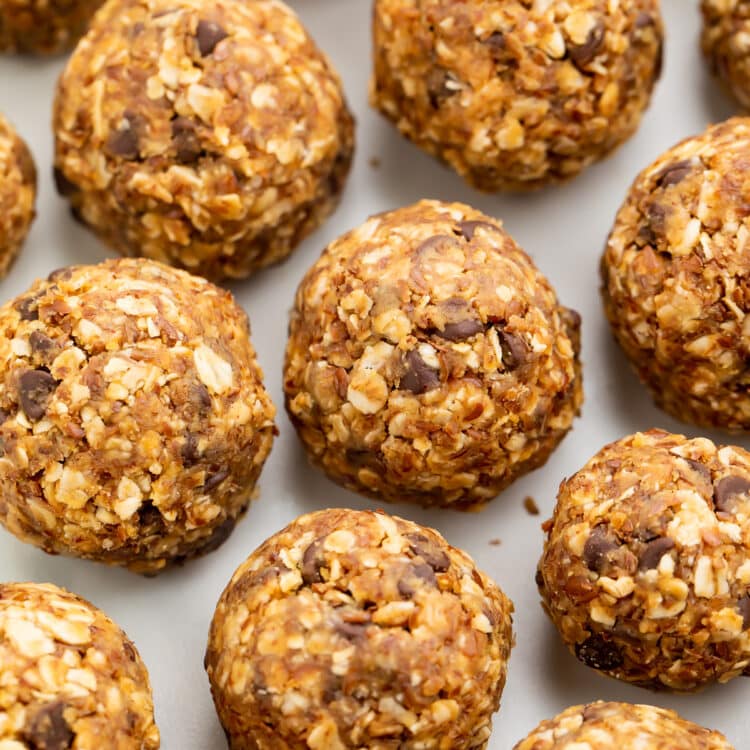 Peanut butter energy bite balls lined up in rows on a sheet of parchment paper.