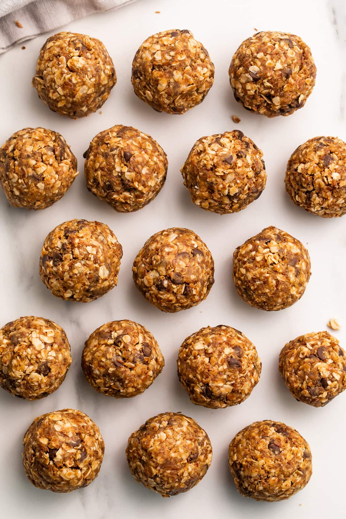 Peanut butter energy bite balls lined up in rows on a sheet of parchment paper.