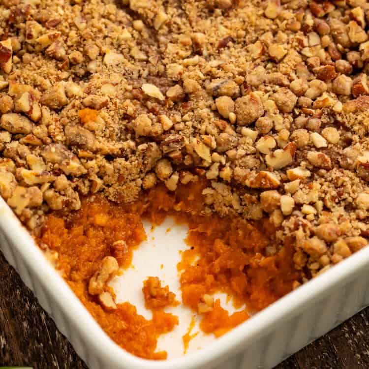 Close up of a sweet potato casserole with a spoonful taken out the corner to show the filling.