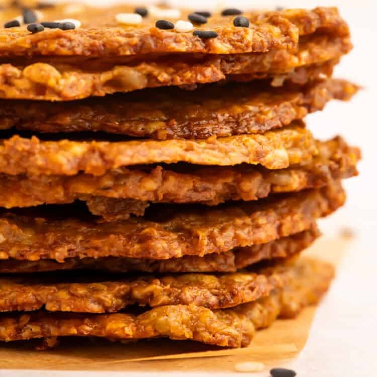 Side-on close up of a stack of avocado chips topped with mixed sesame seeds.