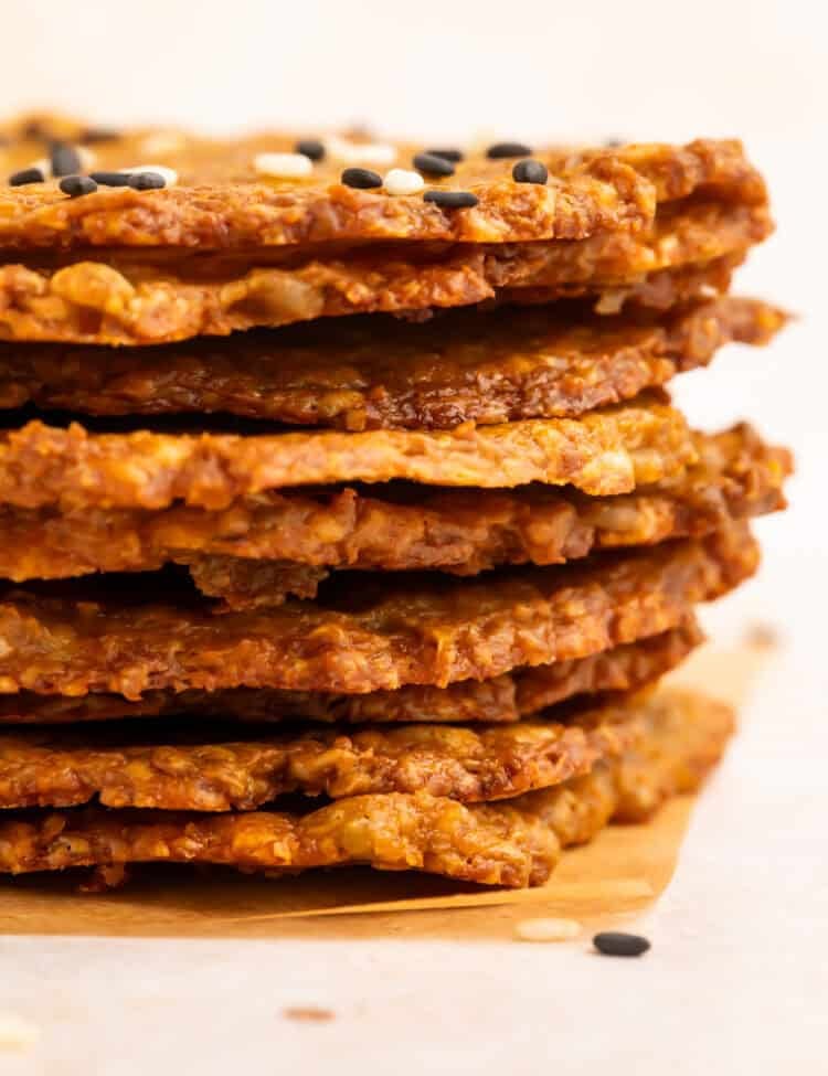 Side-on close up of a stack of avocado chips topped with mixed sesame seeds.