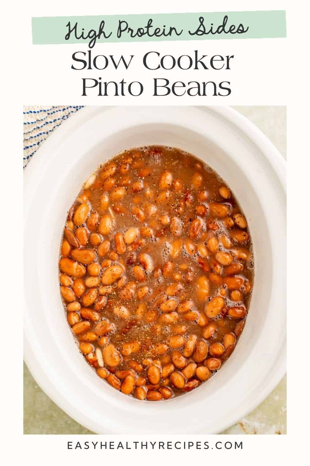 Overhead image of cooked pinto beans in a white slow cooker insert. There is a white frame on the image ith a Pinterest-optimised text overlay.