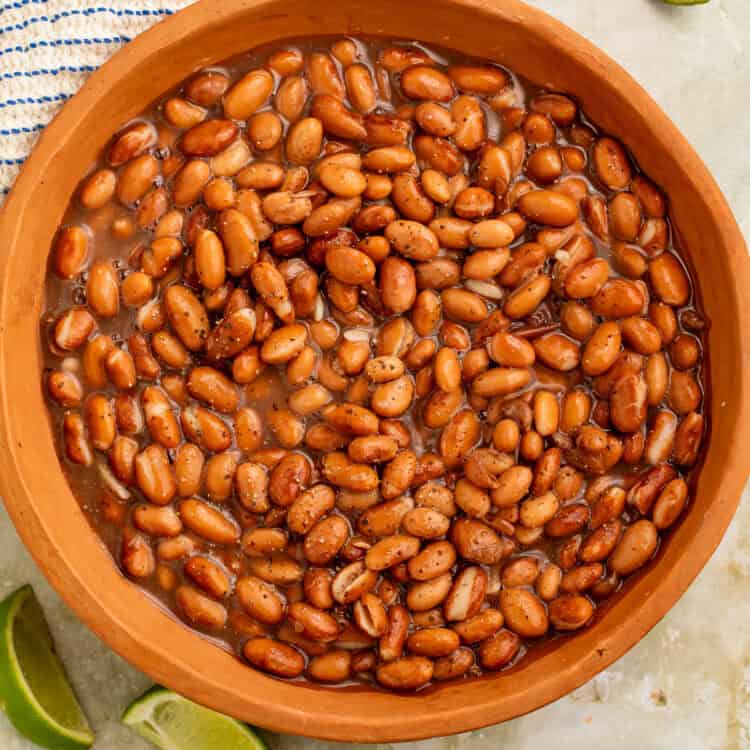 Terracotta bowl of cooked pinto beans with lime wedges on the side.