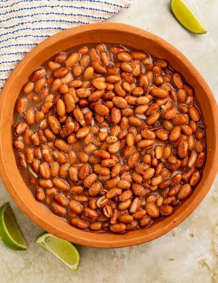Terracotta bowl of cooked pinto beans with lime wedges on the side.