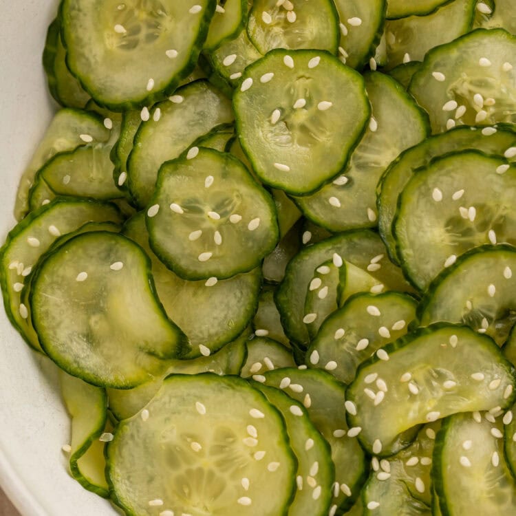 Close up of a sliced cucumber salad in a white bowl with sesame seeds.