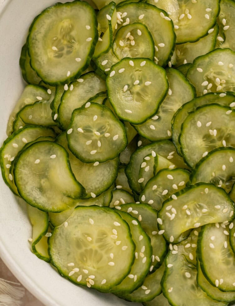 Close up of a sliced cucumber salad in a white bowl with sesame seeds.