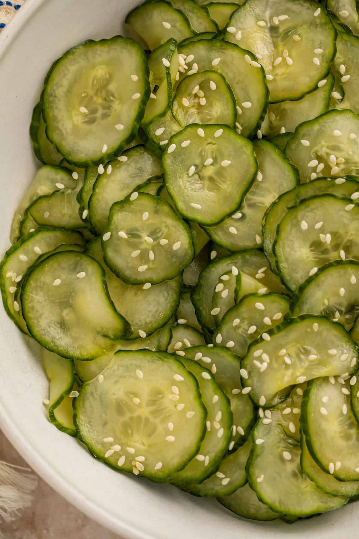 Close up of a sliced cucumber salad in a white bowl with sesame seeds.