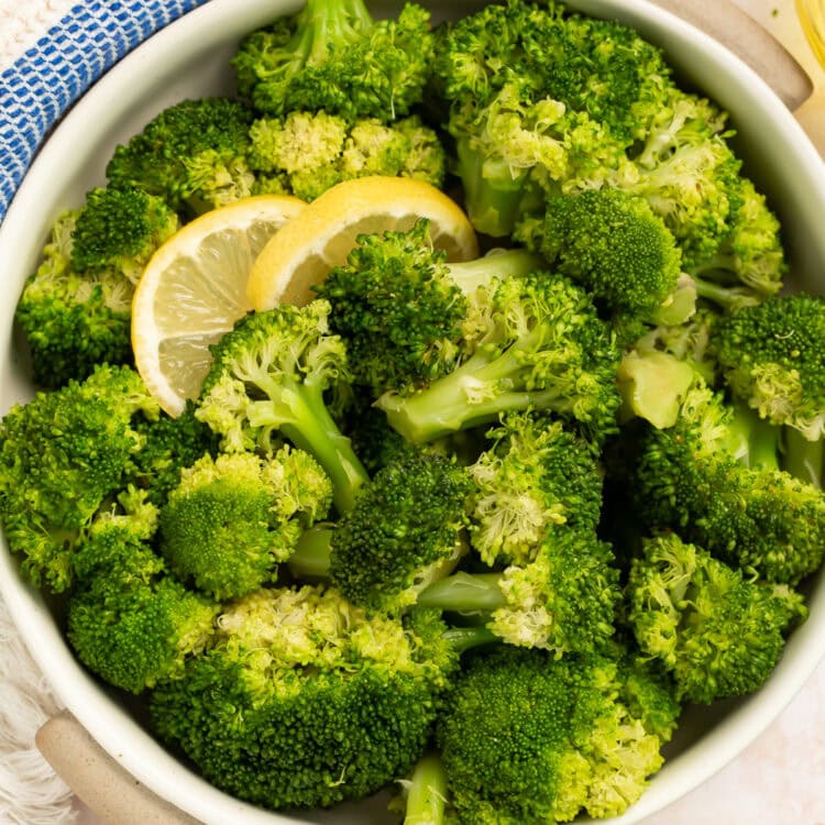 Bowl of cooked broccoli garnished with lemon slices in a white bowl.