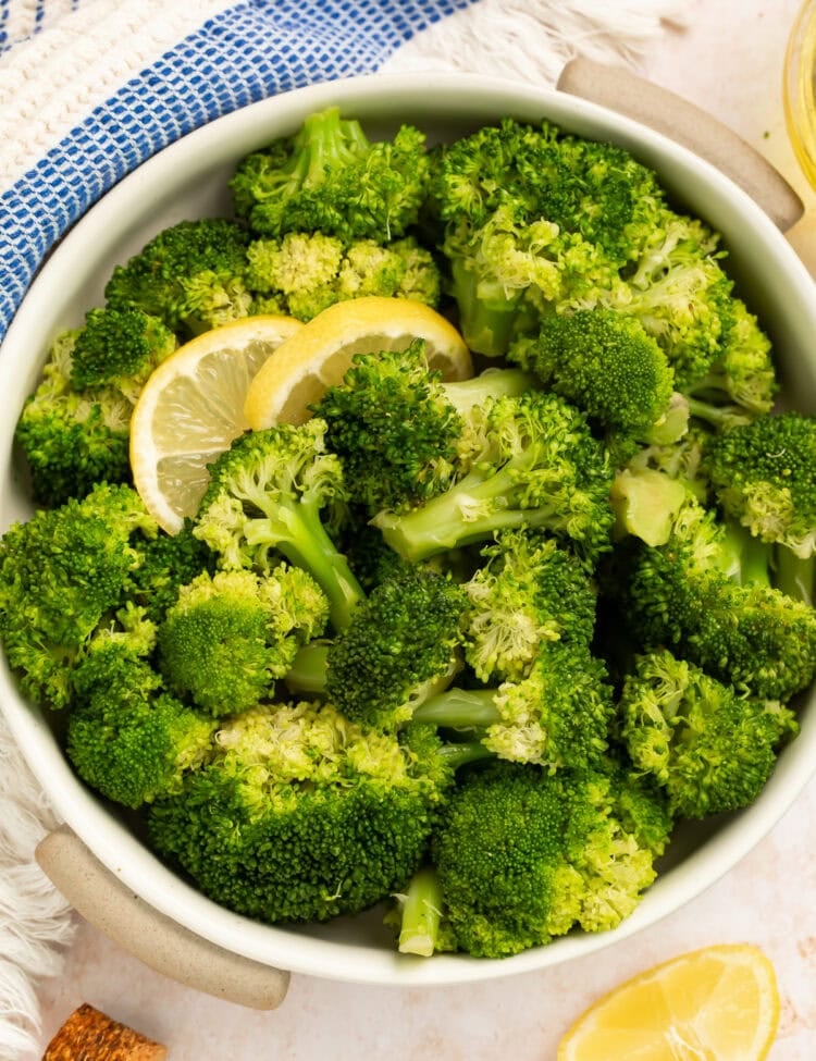 Bowl of cooked broccoli garnished with lemon slices in a white bowl.