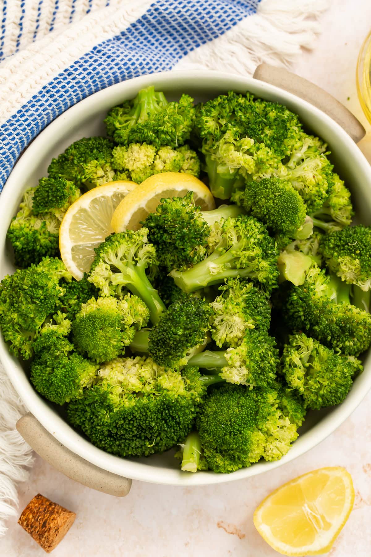 Bowl of cooked broccoli garnished with lemon slices in a white bowl.