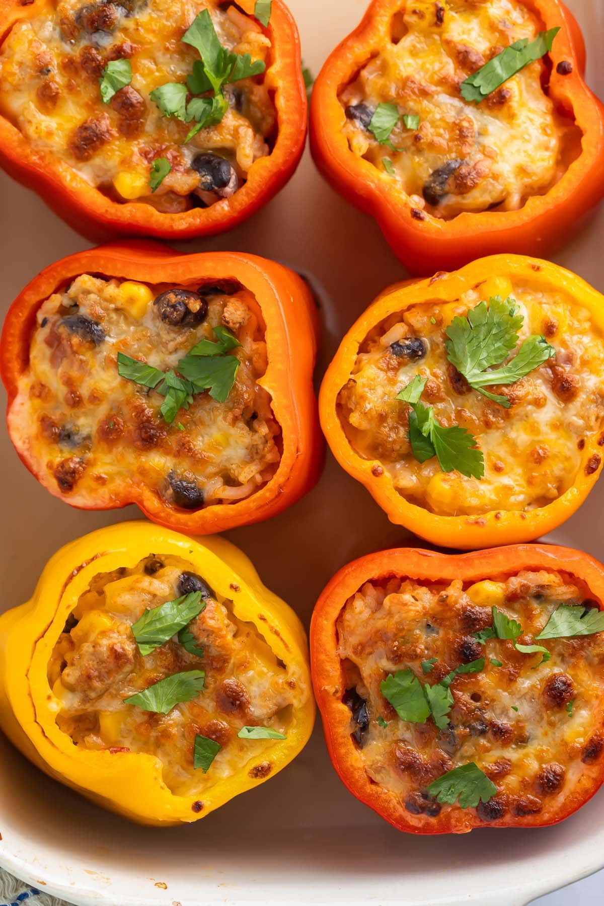 6 Mexican stuffed peppers arranged in 3 rows of 2 in a white casserole dish, photographed from above.