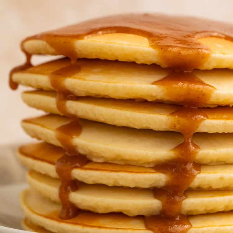Stack of pancakes topped with peanut butter maple syrup running down the sides.