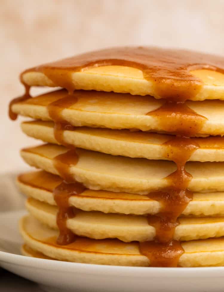 Stack of pancakes topped with peanut butter maple syrup running down the sides.