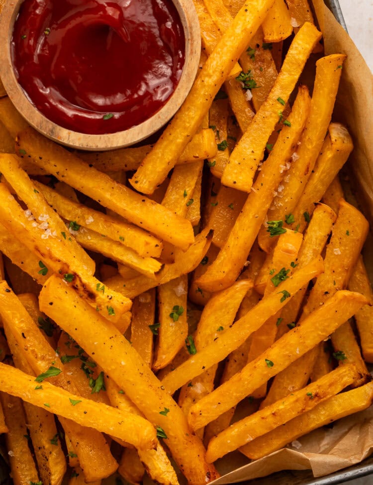 Tray of rutabaga fries with a wooden ketchup bowl nestled amongst them.
