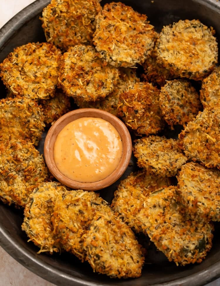 Black bowl of air fryer fried pickles with a small wooden bowl of creamy, spicy dipping sauce.