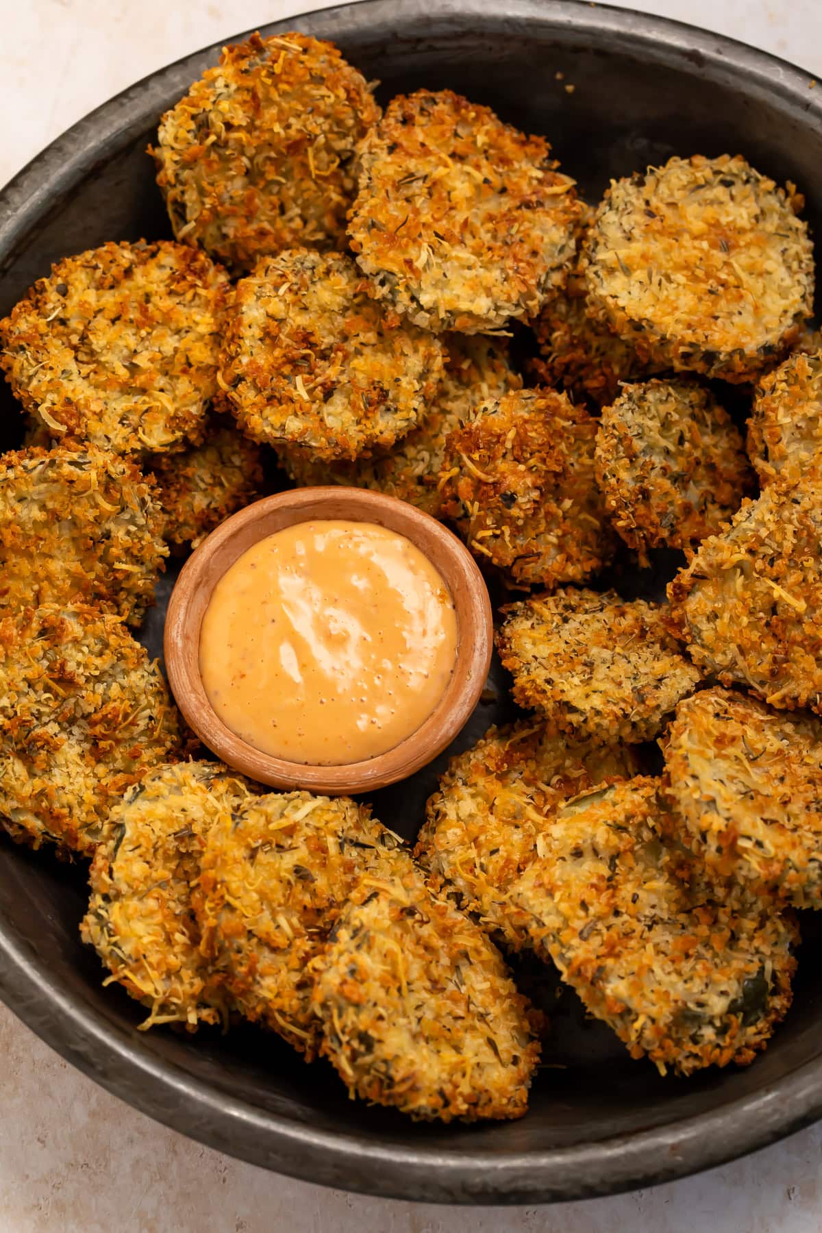 Black bowl of air fryer fried pickles with a small wooden bowl of creamy, spicy dipping sauce.
