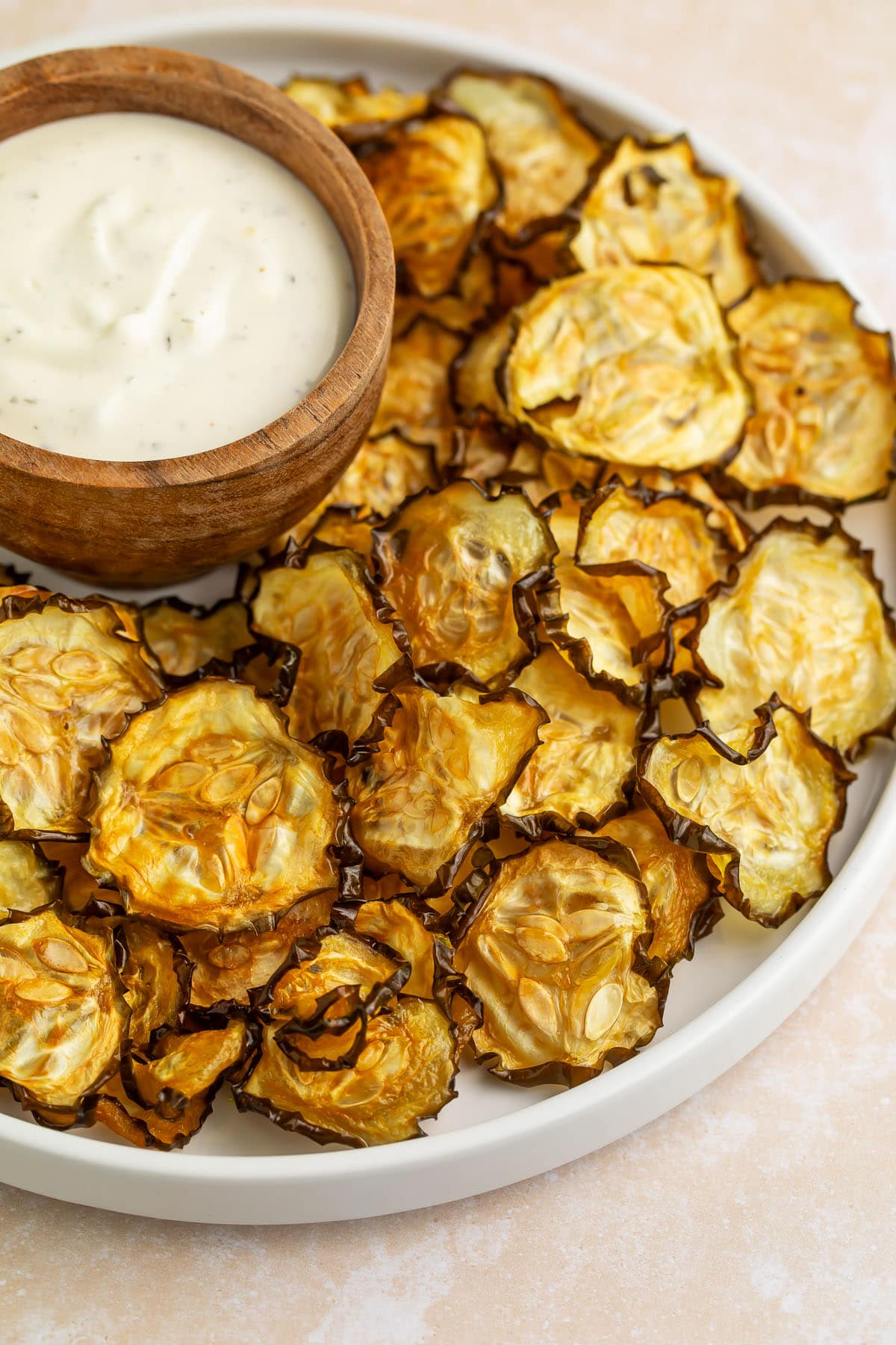 Crispy cucumber chips arranged around a bowl of ranch dressing on a large rimmed plate.