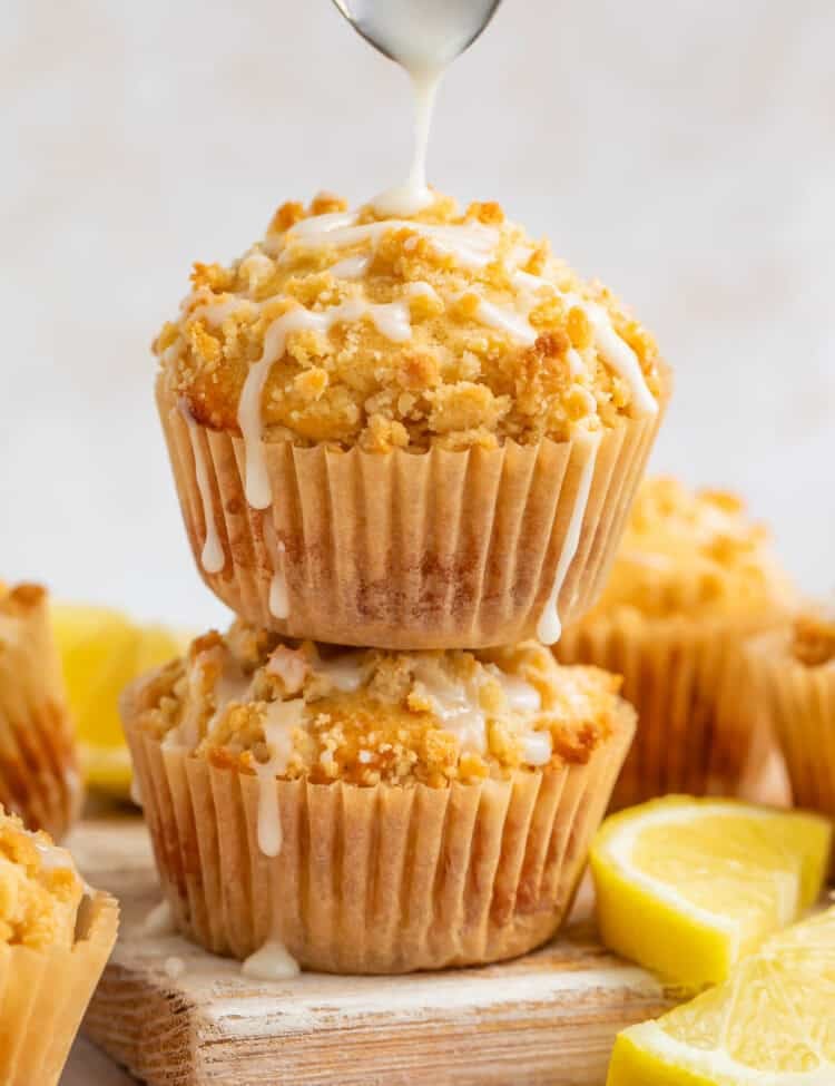 Lemon muffins stacked on top of each other with a spoon drizzling glaze on top.