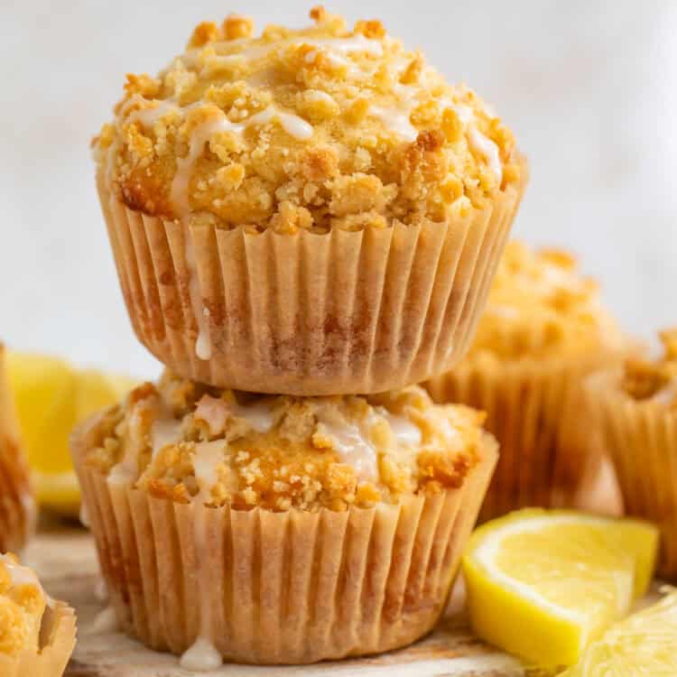 A pair of lemon muffins stacked on top of each other on a serving board with lemon wedges.