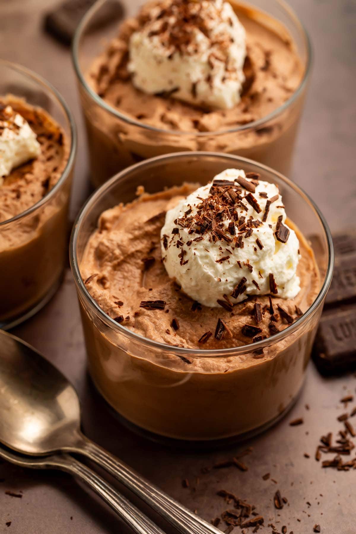 Three glass cups of keto chocolate mousse topped with keto whipped cream and chocolate shavings.