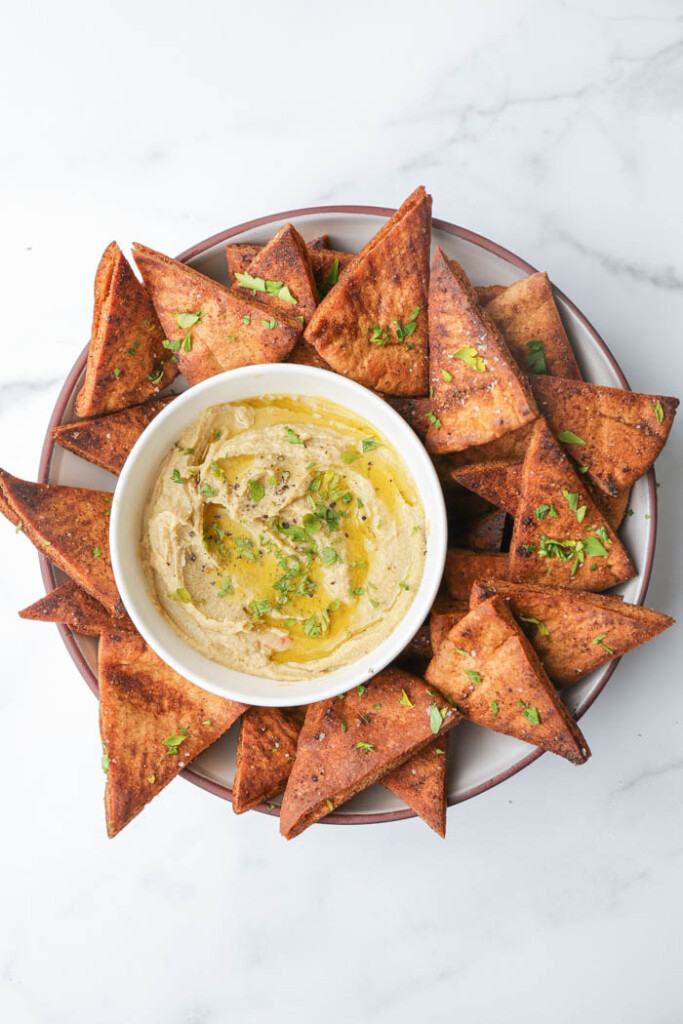 Overhead of a bowl of hummus surrounded by homemade pita chips
