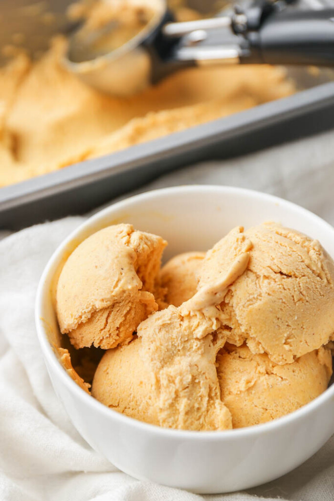 A bowl of pumpkin ice cream with a tray of it in the background