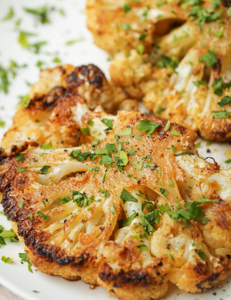 Roasted cauliflower steaks on a white plate garnished with parsley.