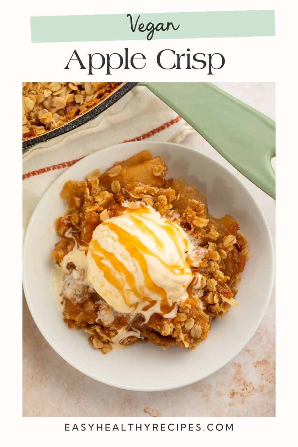 White bowl of apple crisp topped with a scoop of vanilla ice cream and drizzled with caramel. There is Pinterest overlay text in a frame around the image.